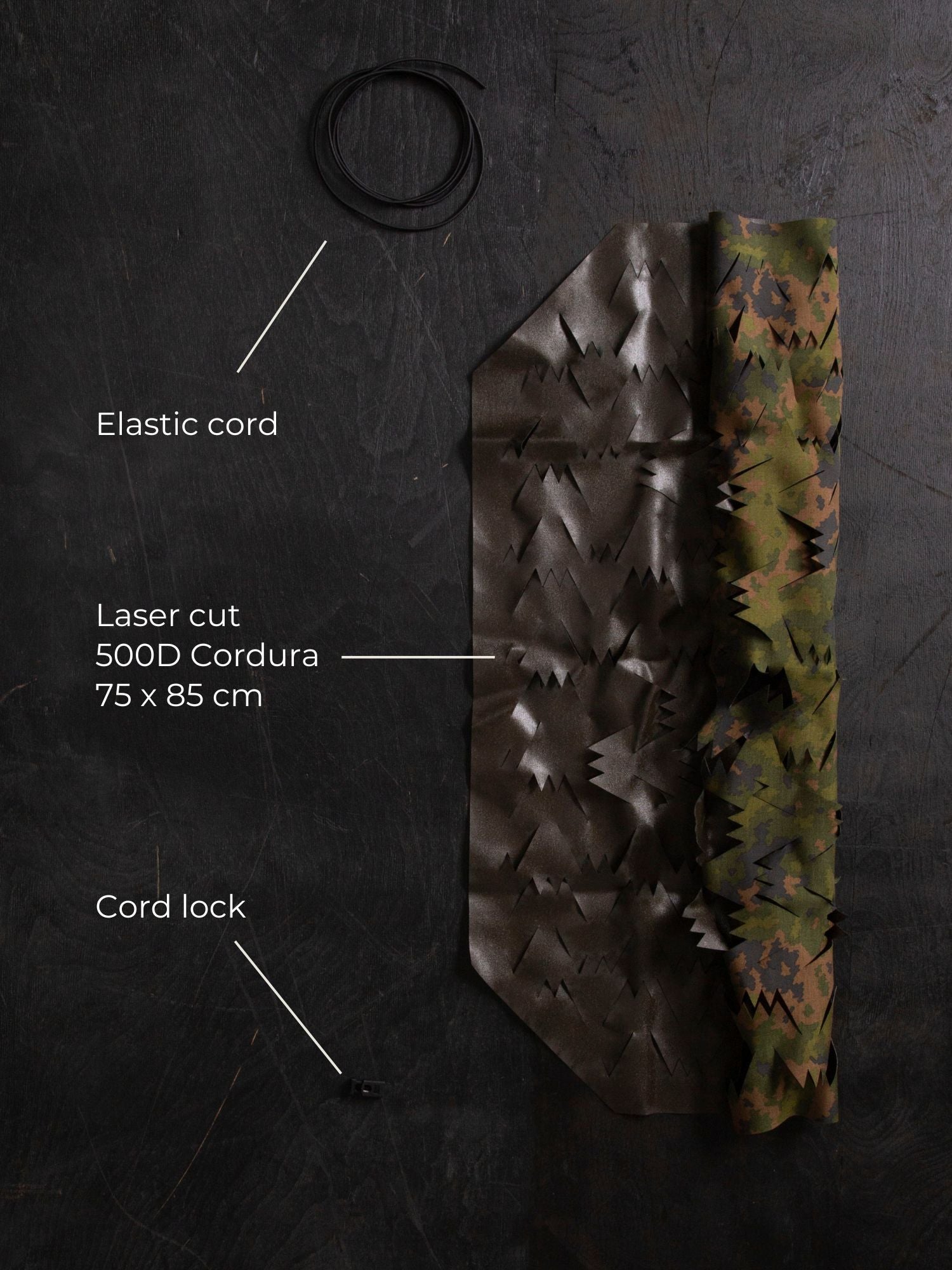 Technical image of the materials of the Savotta Backpack camo scrim 15-30L. There are Laser cut 500D Cordura 75 x 85cm, elastic cord and a cord lock on a black wooden surface.