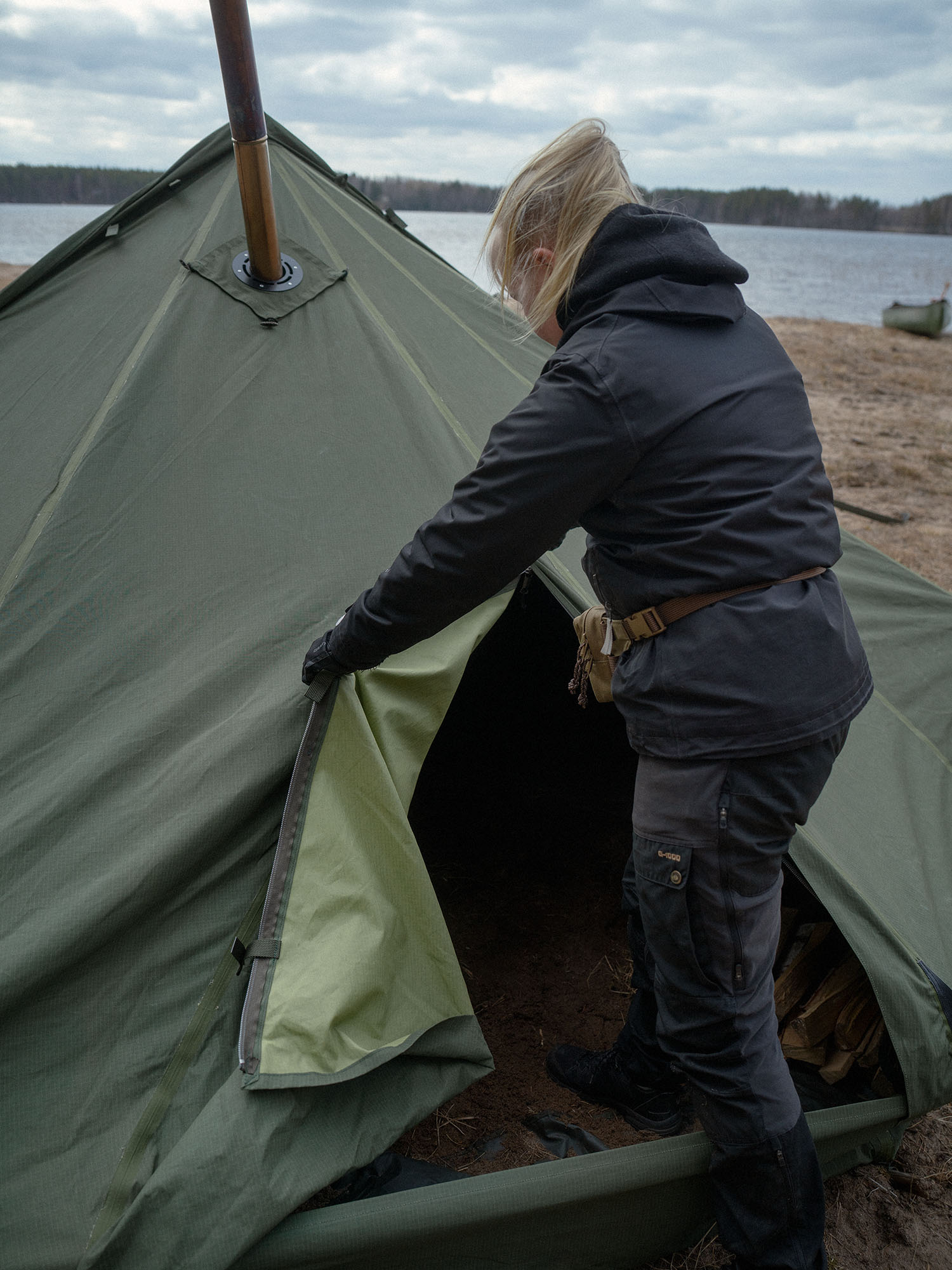 Person setting up a Savotta Hawu 8 tent by a lake