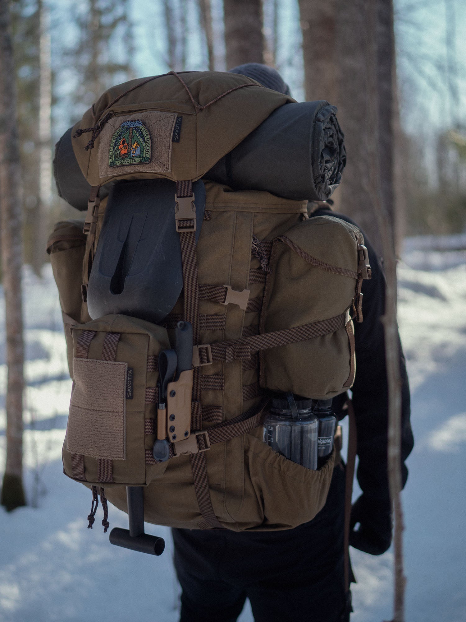 Person with a large brown Savotta Kantamus 60L backpack with Lidded GP pouches and Rintamus chest pack attached on the outside, in a snowy forest