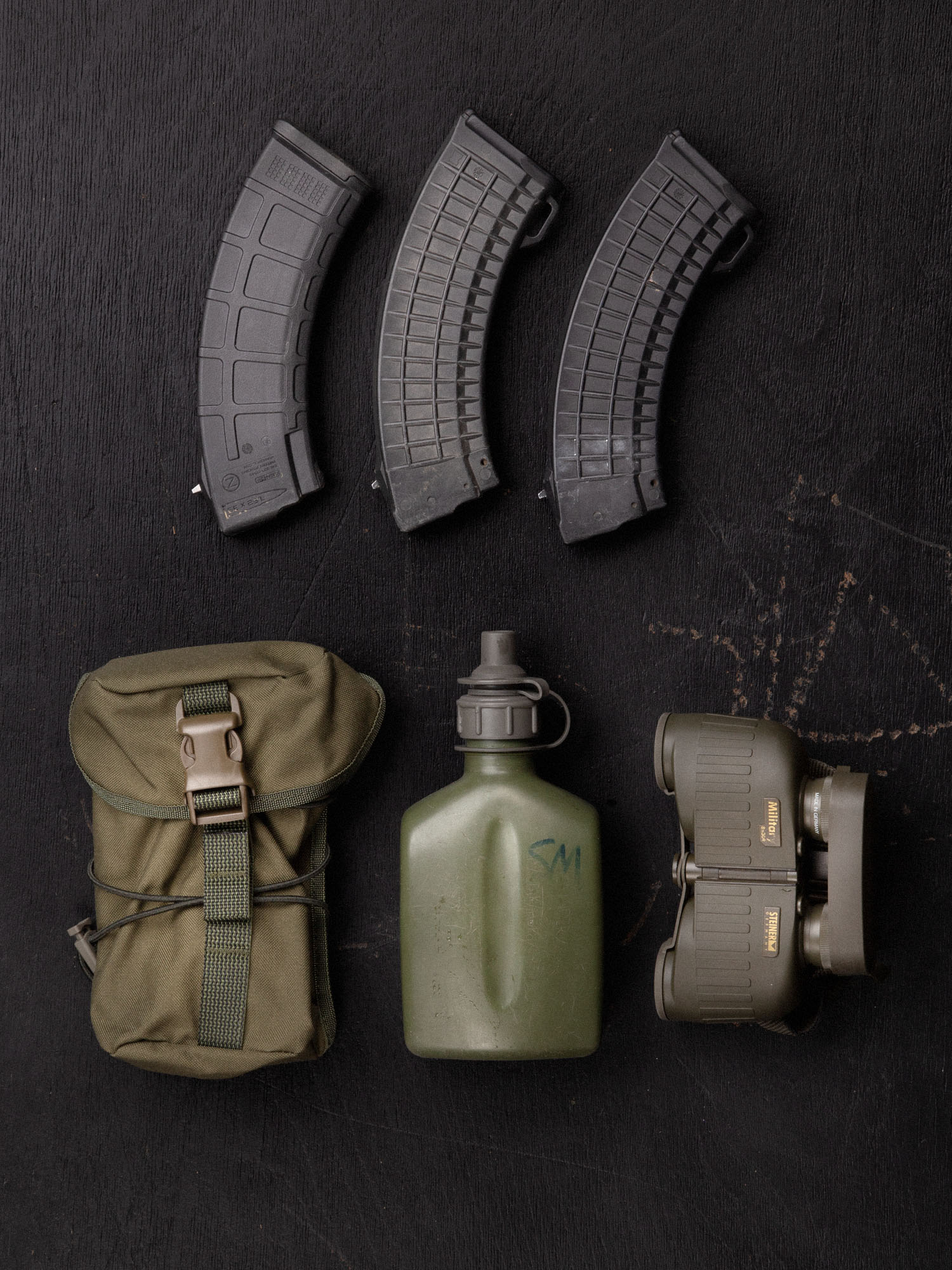 Savotta Lidded GP pouch 3x4 and a set of military supplies that fit into the pouch including magazines, a canteen, and binoculars on a dark wooden surface.