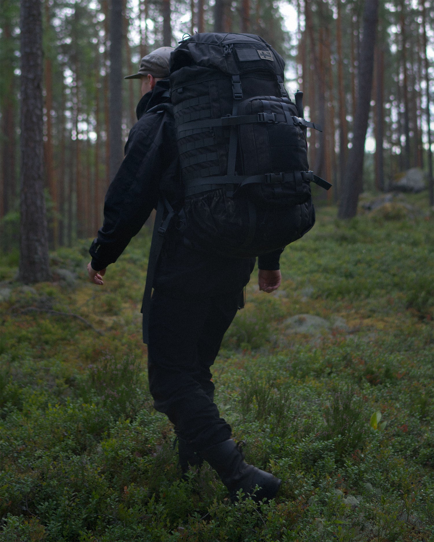 Person with a black Kantamus 60L backpack with a Savotta Askare hip pack attached walking through a forest