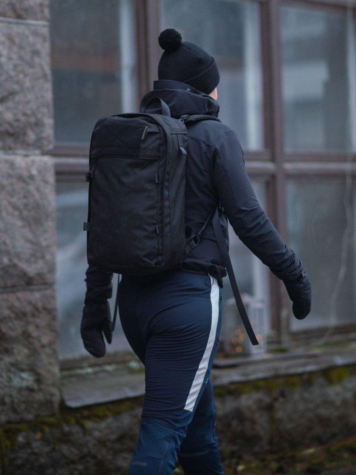 Sporty person wearing a black Savotta Niukka 20L backpack and black outdoor clothing walking outdoors.