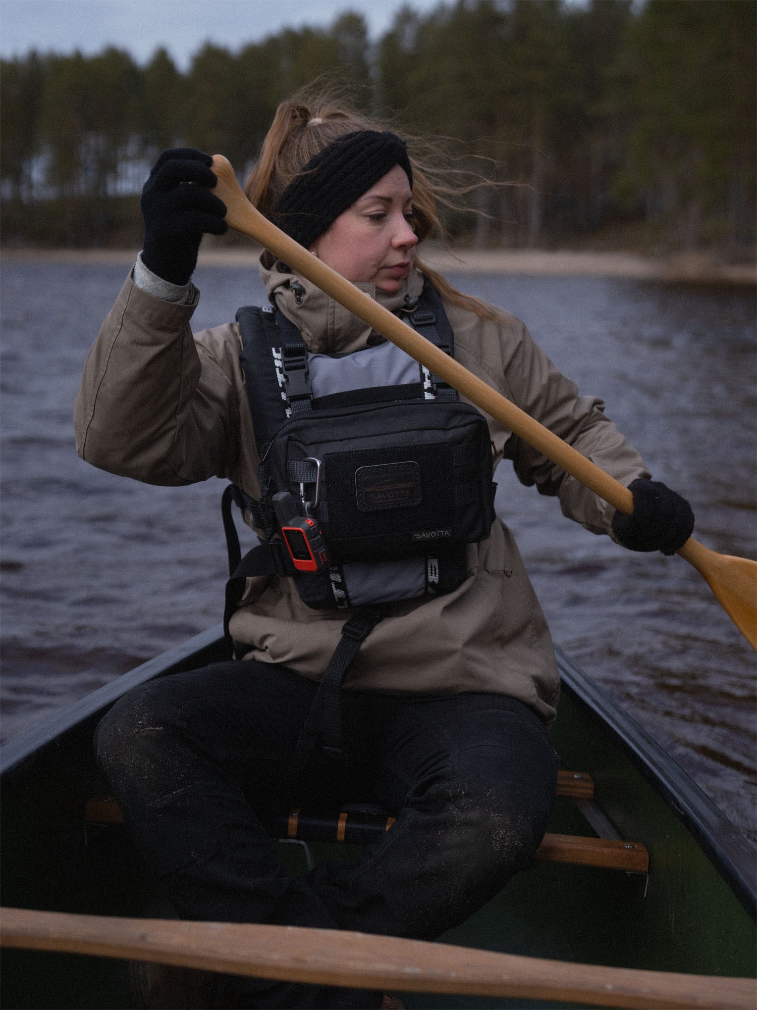 Person paddling a canoe on a lake with a forest in the background, wearing a black Savotta Rintamus chest pack with a black Savotta leather patch