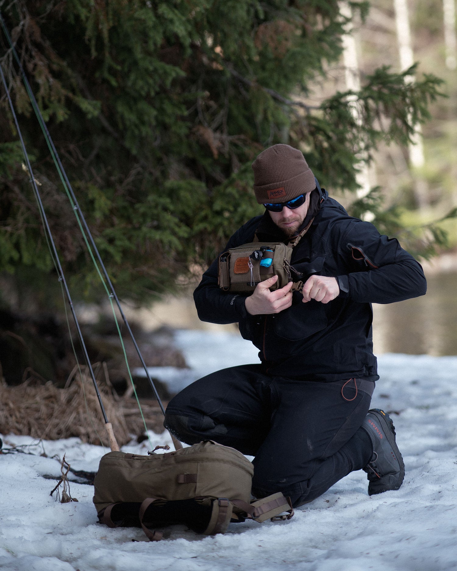 Person in winter clothing setting up Savotta Rintamus chest pack in a snowy forest with Savotta Niukka 20l on the ground.