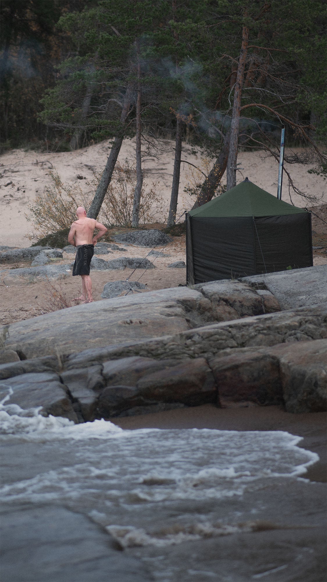 Man standing on a rocky beach with a Savotta Hiisi 4 sauna tent in the background