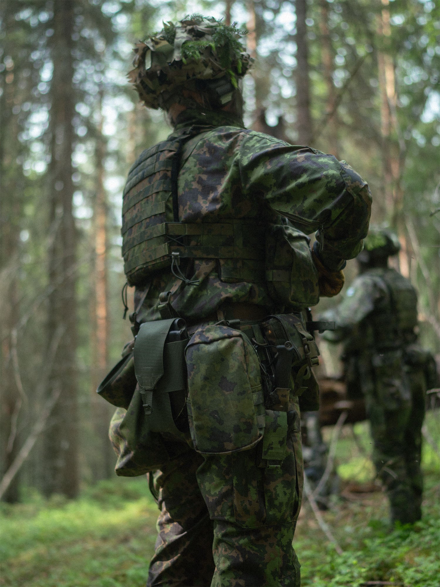 Person in camouflage military uniform with a Savotta trifold E-tool pouch attached to the waist, standing in a forest