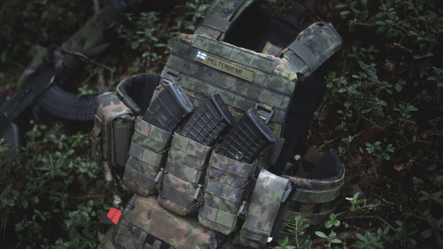 Savotta Varjelus plate carrier in M05 woodland with multiple Open top magazine pouches for AK/RK or AR15 magazines on a grassy background
