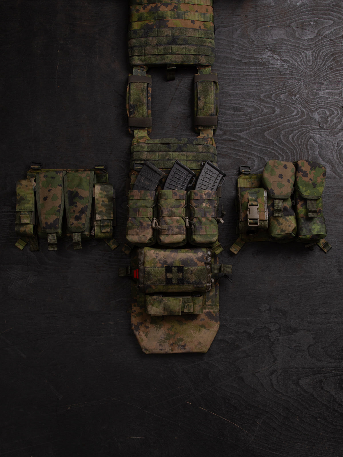 Savotta Varjelus PALS placard and different Savotta mag pouches attached to the Varjelus plate carrier which is being spread out on a dark wooden background.