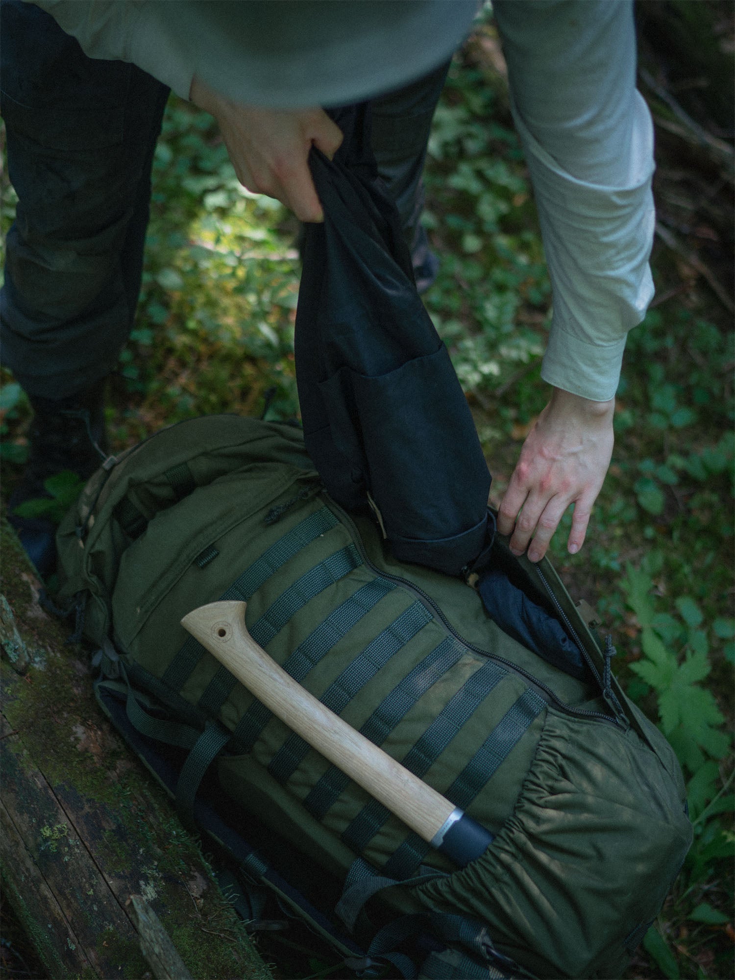 Person taking a jacket out of the front zipper pouch of a flat compartment of the Savotta Kantamus 60L on a forest floor