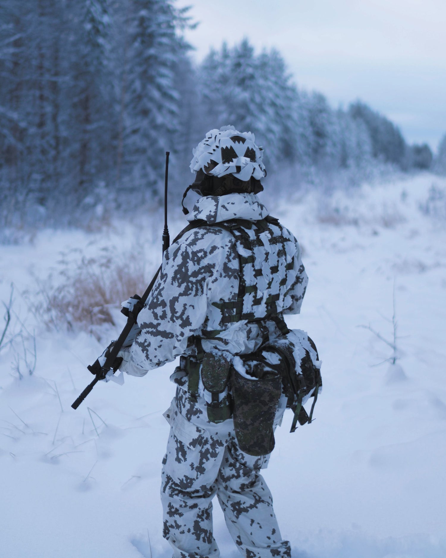 Person in winter camouflage gear standing in a snowy forest