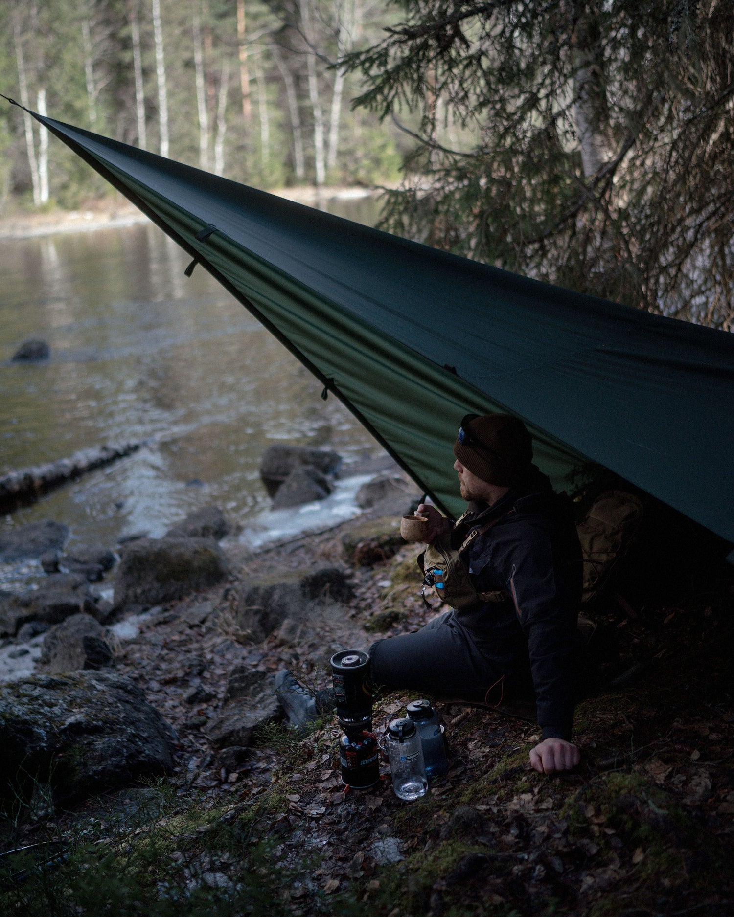 Person camping by a lake with a Savotta Laavu tarp as shelter