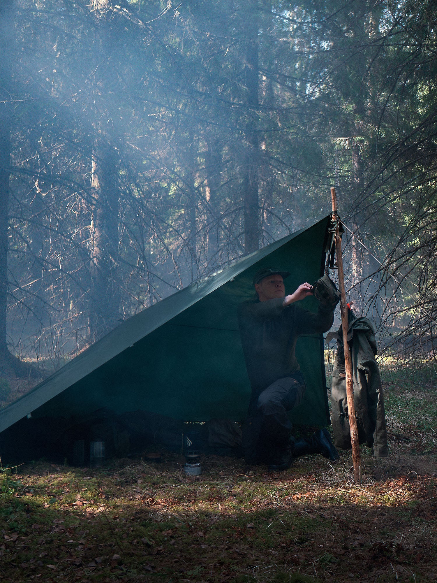 Person sitting under a Savotta Laavu tarp in a Finnish forest.