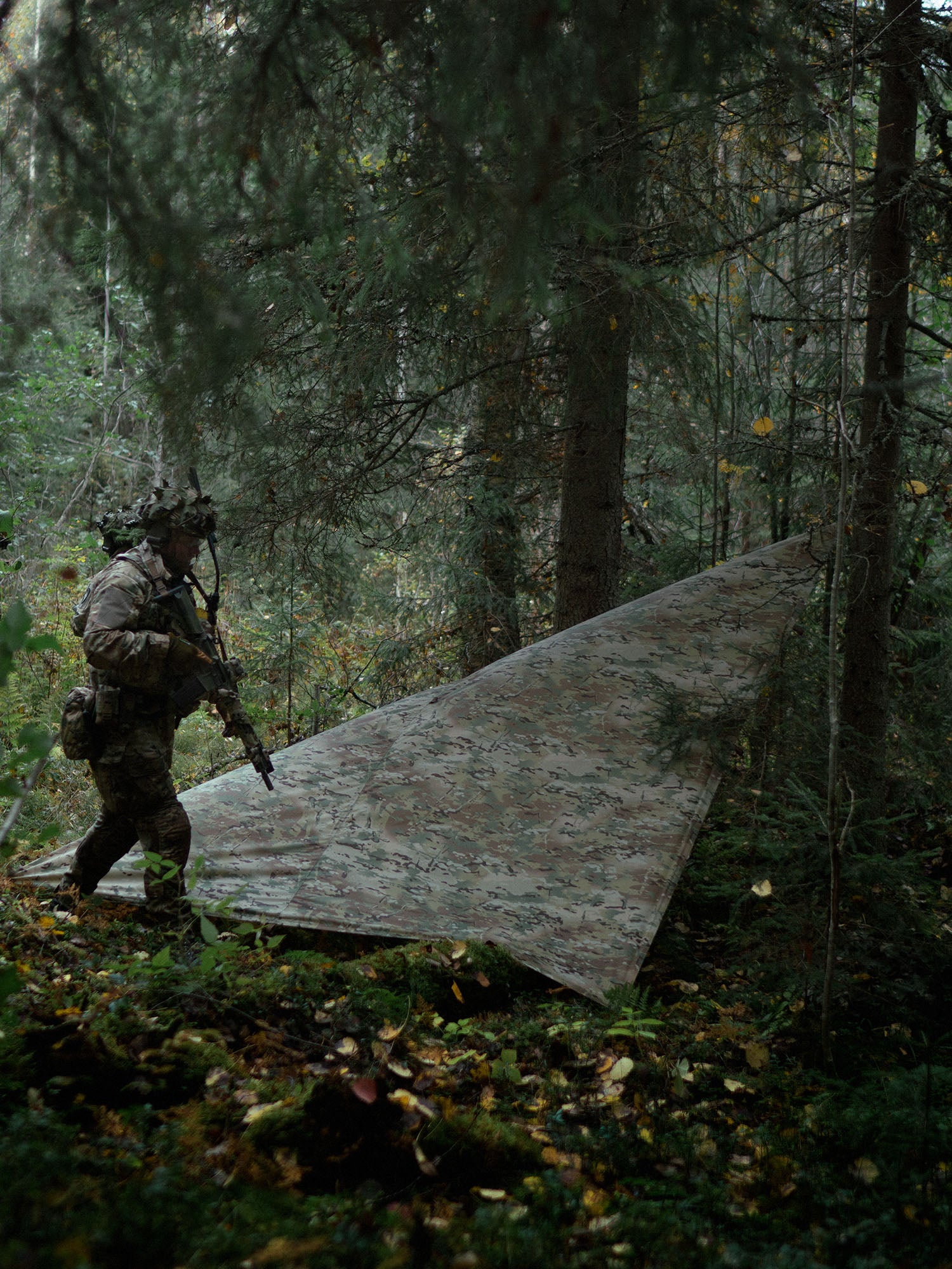 Person in camouflage gear walking by a Savotta Multicam Laavu tarp in a forest
