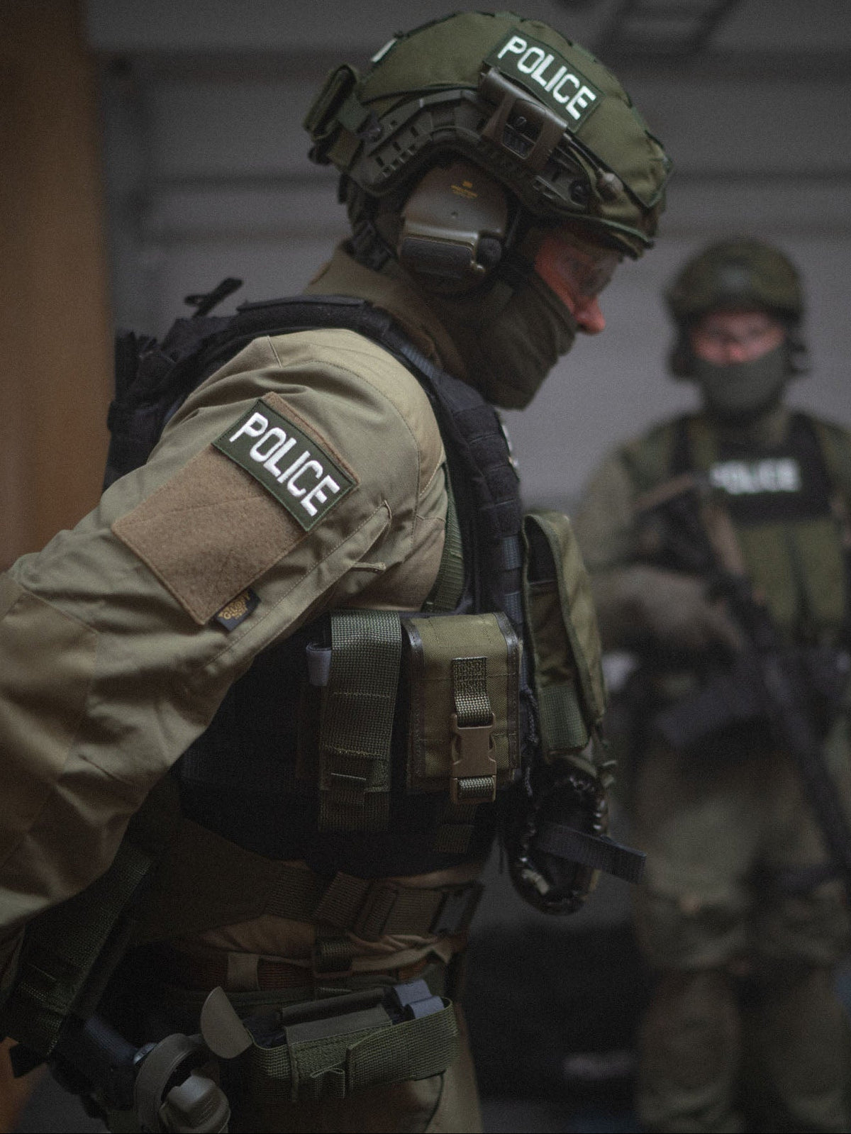Two police officers in tactical gear with 'POLICE' on their helmets and uniforms. One of them has a Savotta tourniquet pouch and a Savotta frag-smoke pouch attached to the vest.