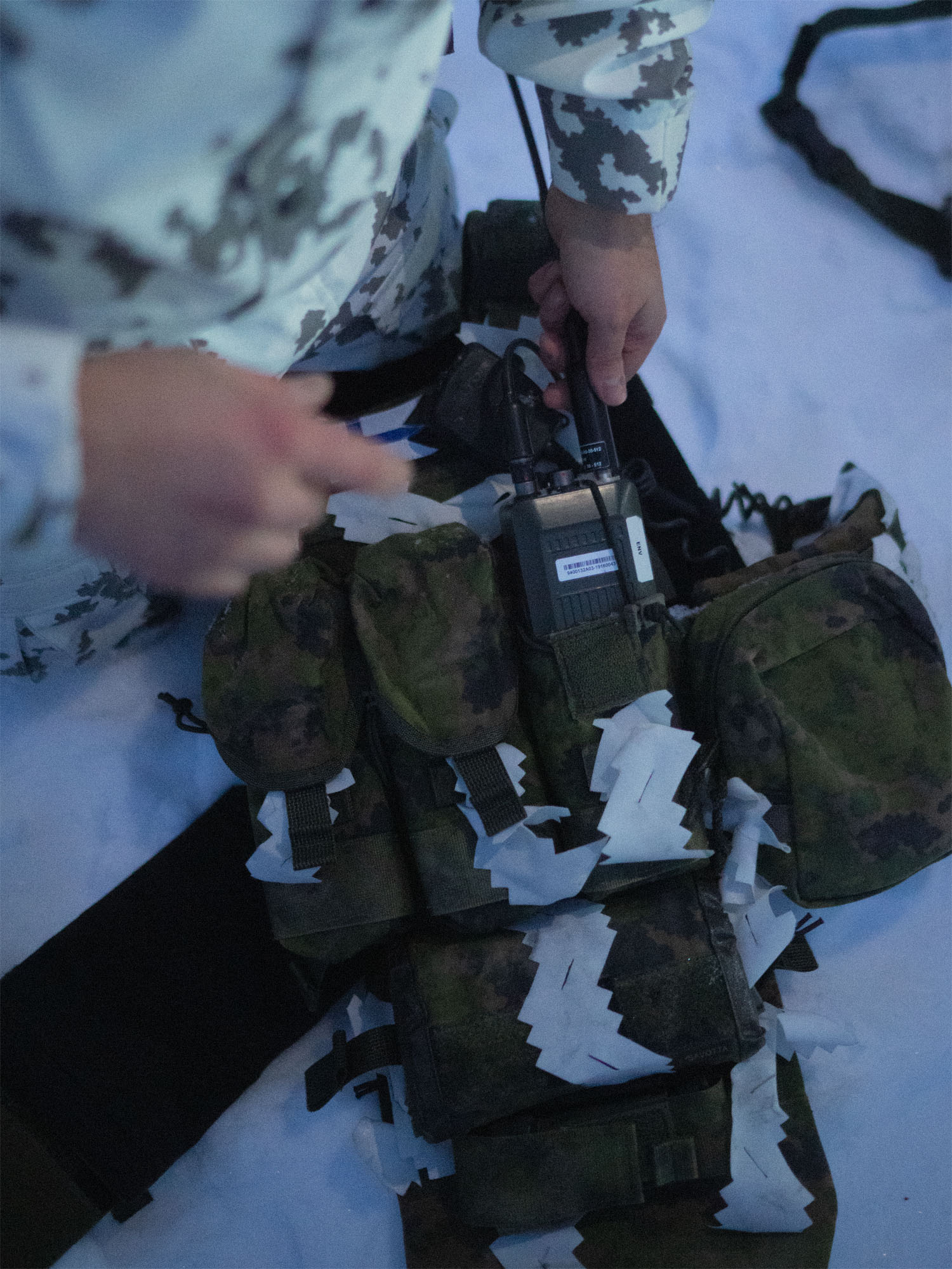 A soldier handling the Savotta Varjelus plate carrier with Varjelus 3x2 AR15-AK placard and groin flap attached in a snowy setting