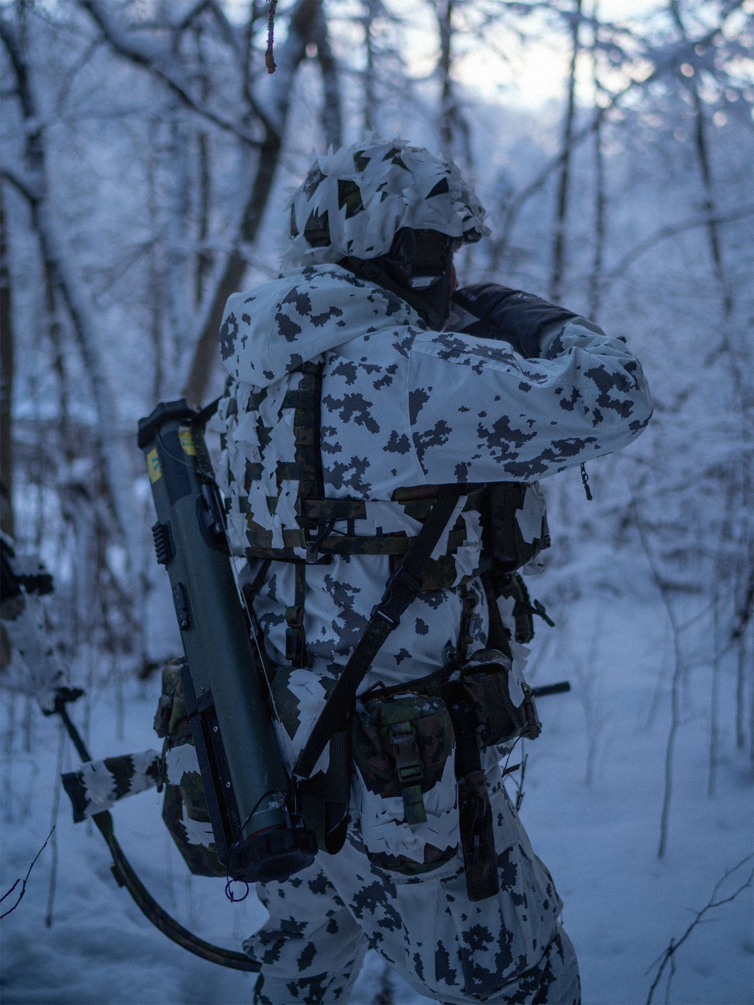 Person in camouflage gear wearing Savotta Varjelus Plate Carrier in a snowy forest.