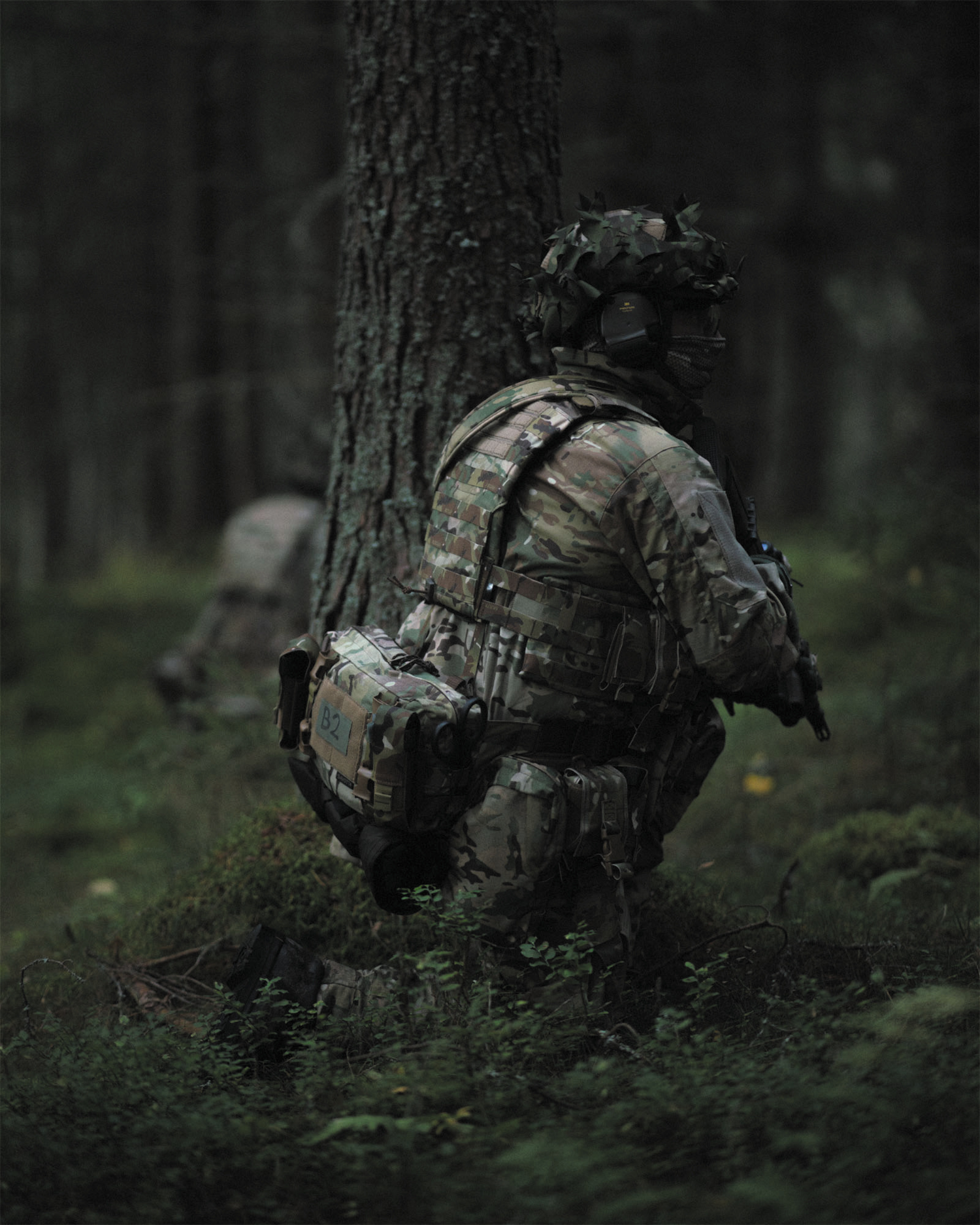 Person in camouflage gear hiding behind a tree in a forest