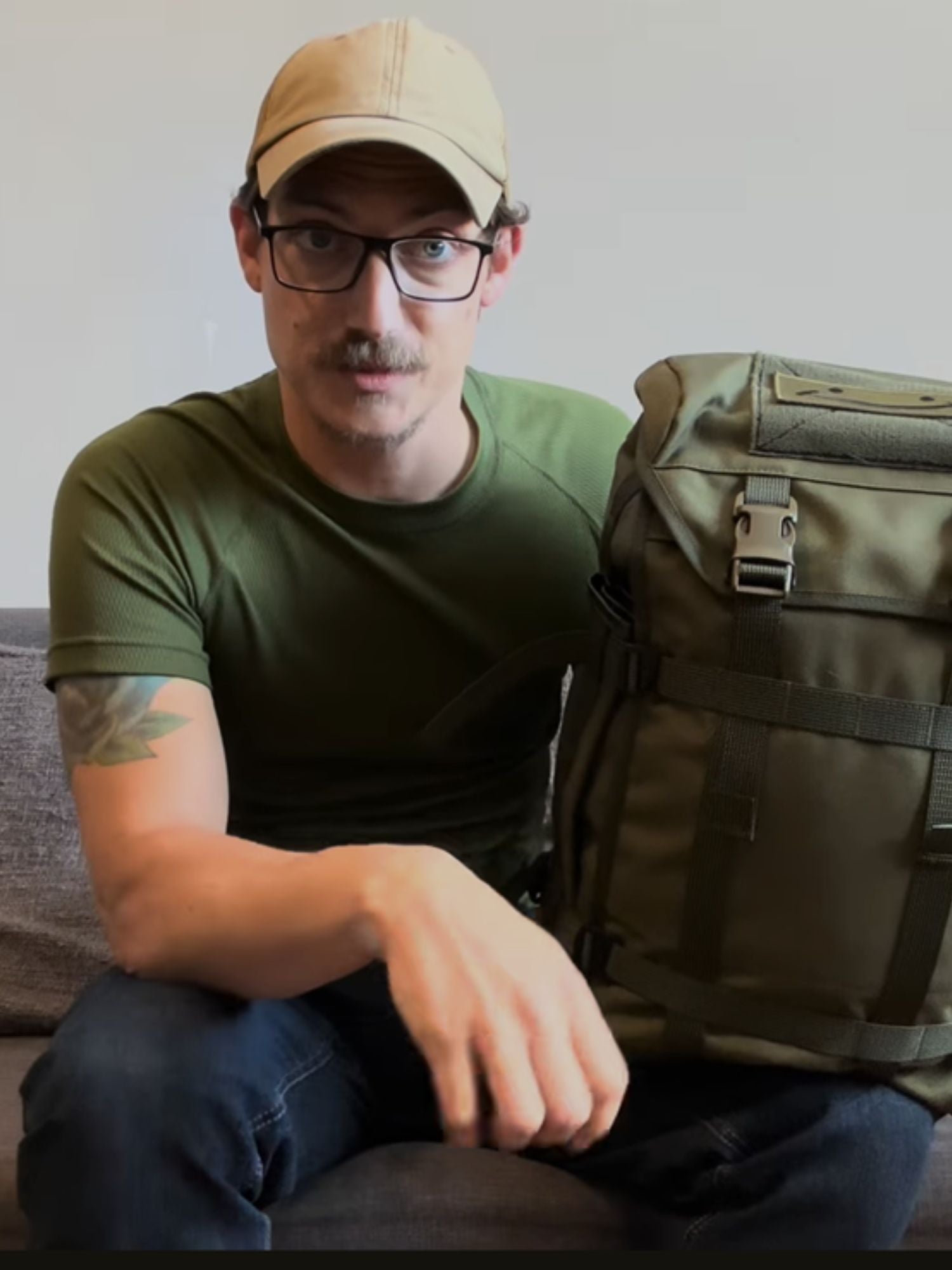 Man wearing a green shirt and beige cap sitting next to a green Savotta Kahakka 25L backpack.