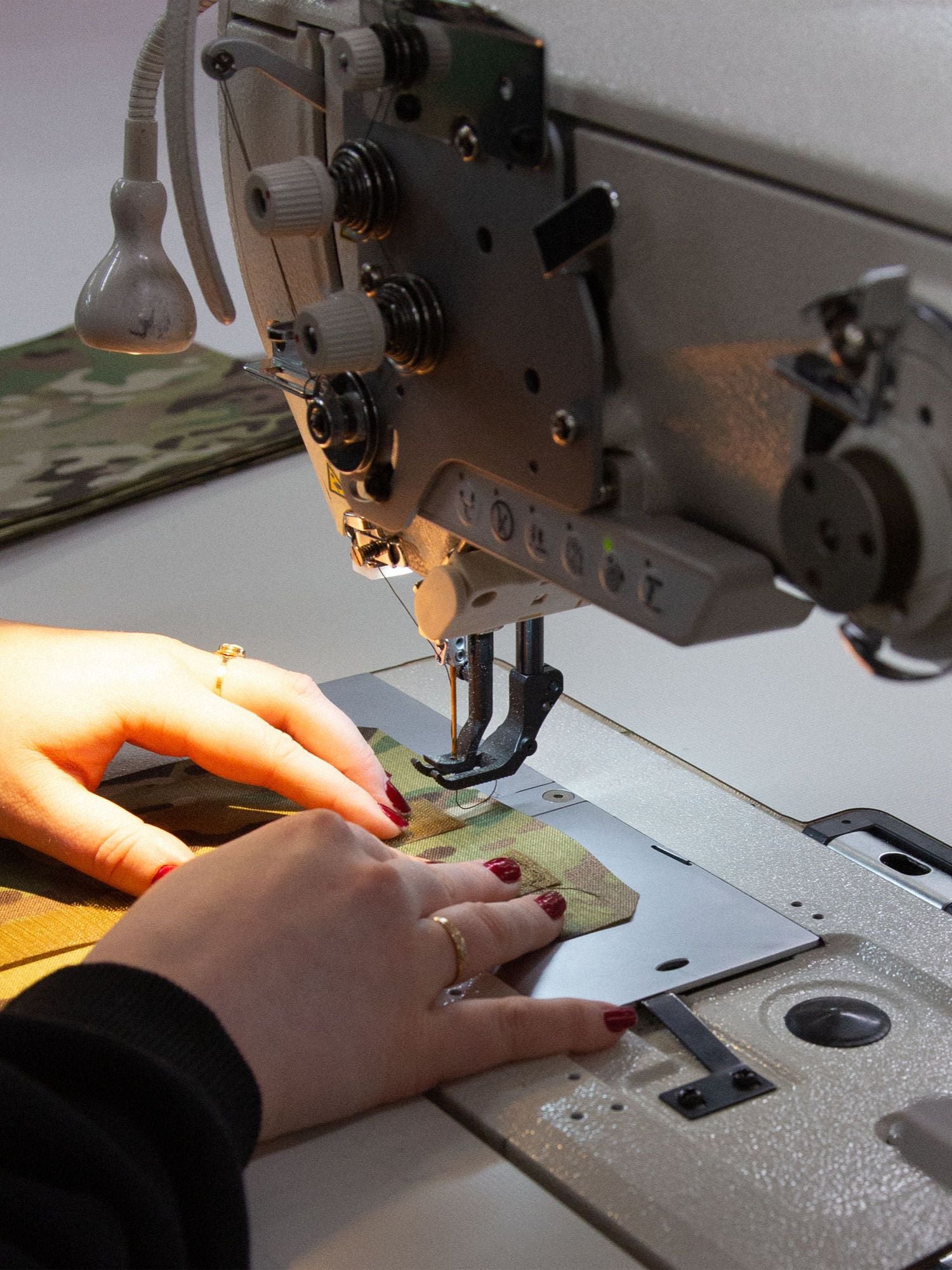 Person using a sewing machine on a piece of fabric with Multicam camouflage pattern.