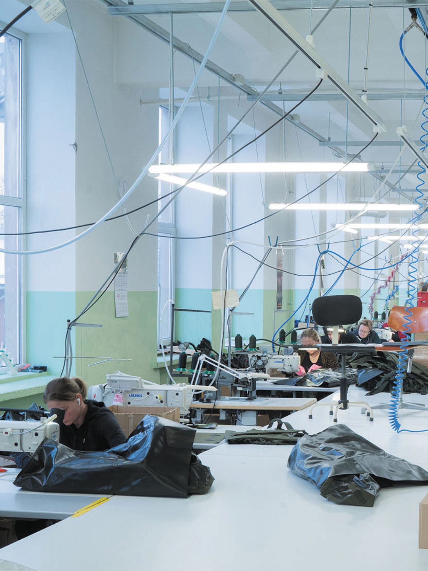 Factory interior with workers at their sewing stations, surrounded by machinery and equipment.