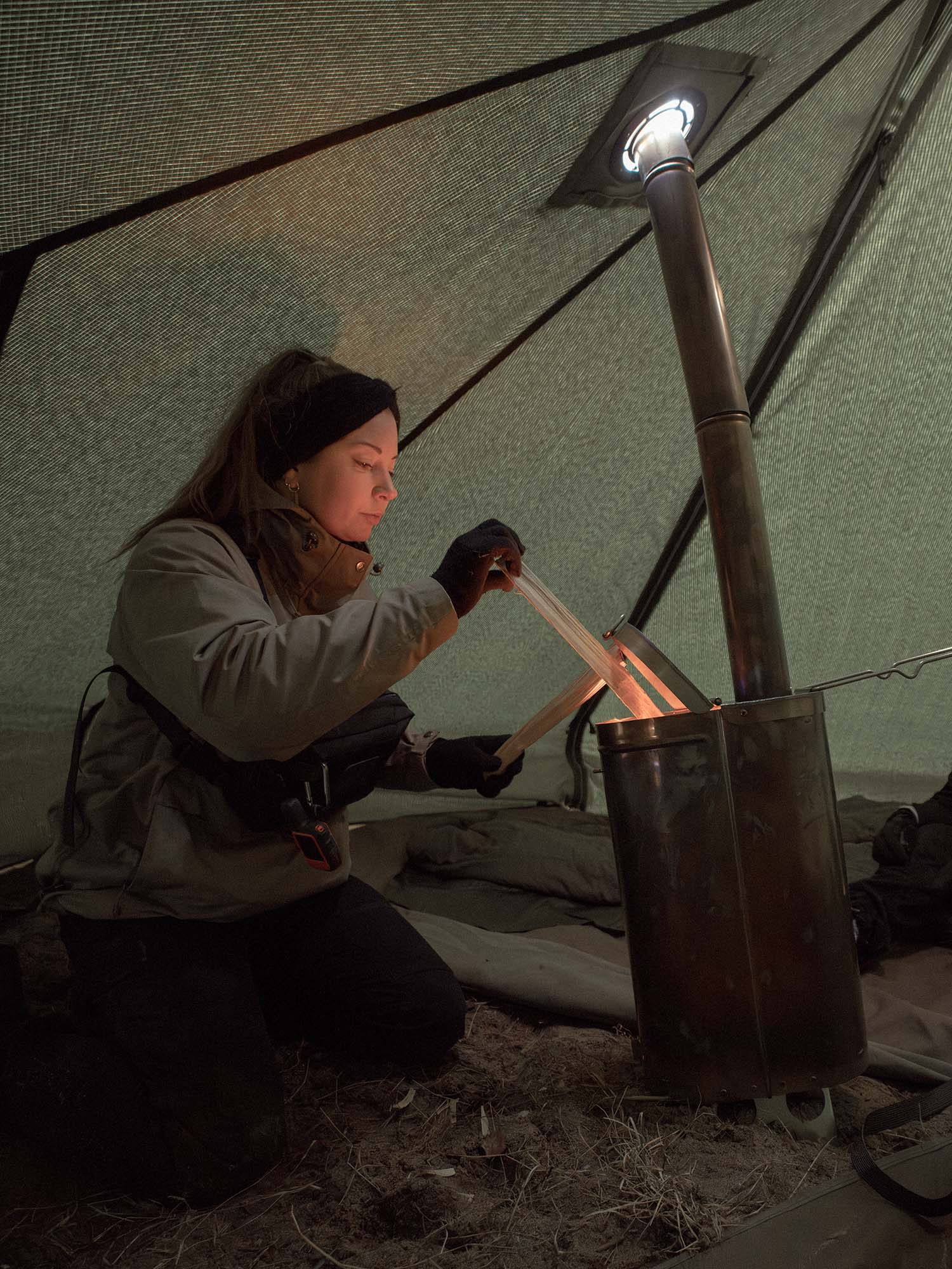Person adding firewood into Savotta Hawu 8 stove inside a tent