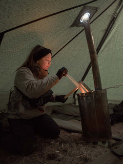 Person adding firewood into Savotta Hawu 8 stove inside a tent