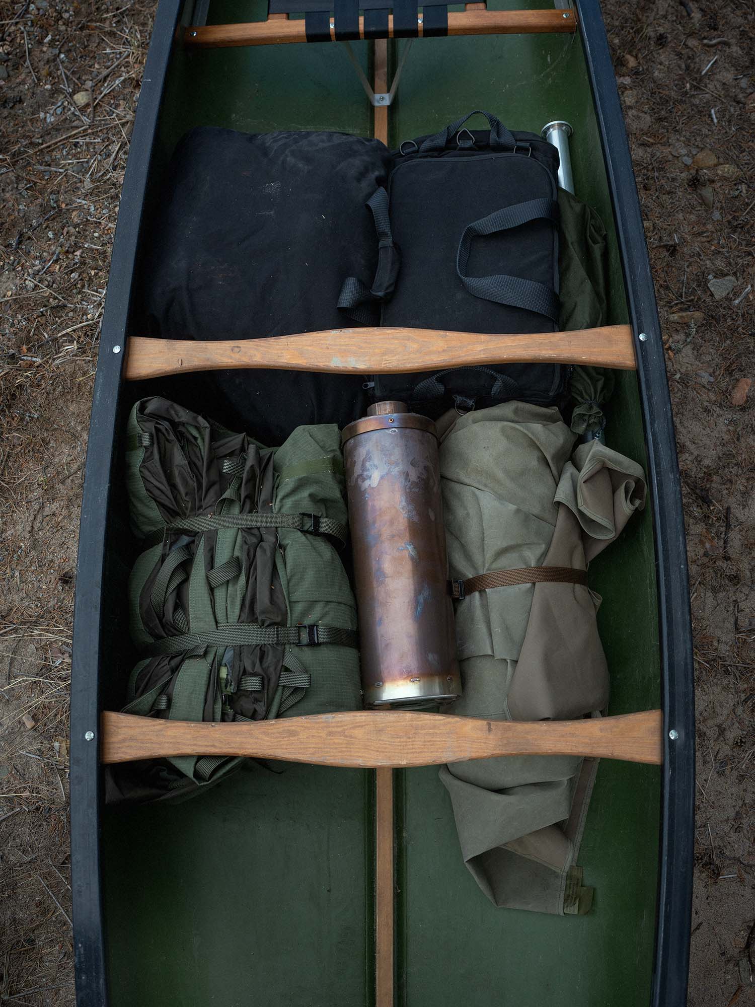 Green canoe with camping gear including Savotta Hawu 8 tent, groundsheet, stove, tent stake set and center pole