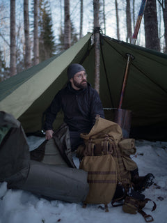 A man setting up camp and Savotta Hawu 8 tent in a snowy forest with camping gear around him