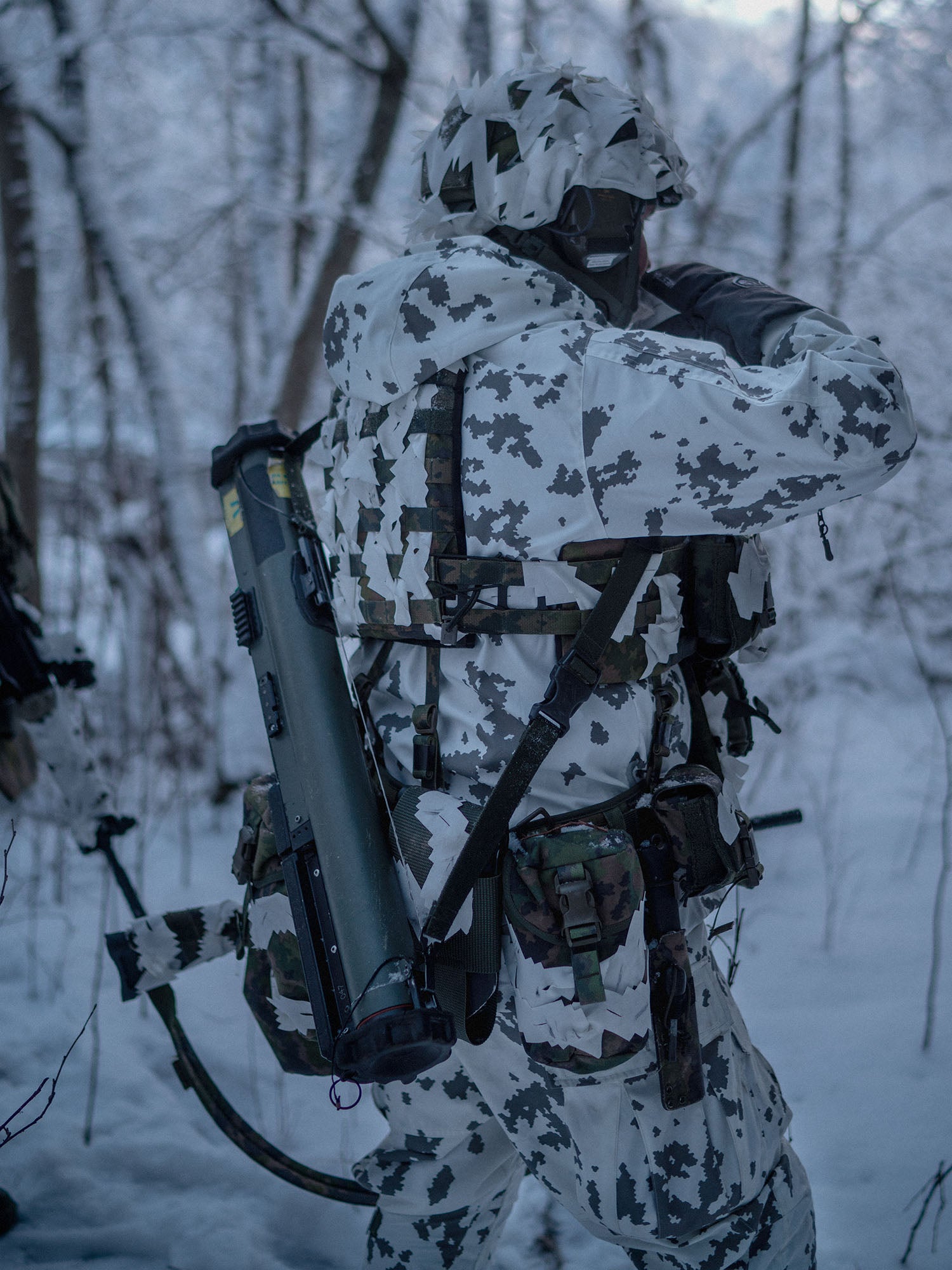 Person in camouflage gear with a large weapon and a Savotta Lidded GP pouch 3x4 attached to the waist in a snowy forest