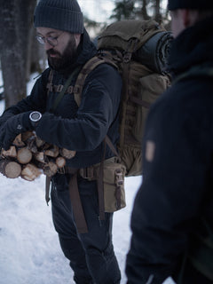 Person wearing a backpack with a Savotta Lidded GP pouch 3x4 attached, holding firewood in a snowy setting