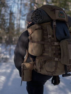 Person with a Savotta Kantamus backpack with a Savotta Lidded GP pouch 4x5 attached and camping gear walking in a snowy forest