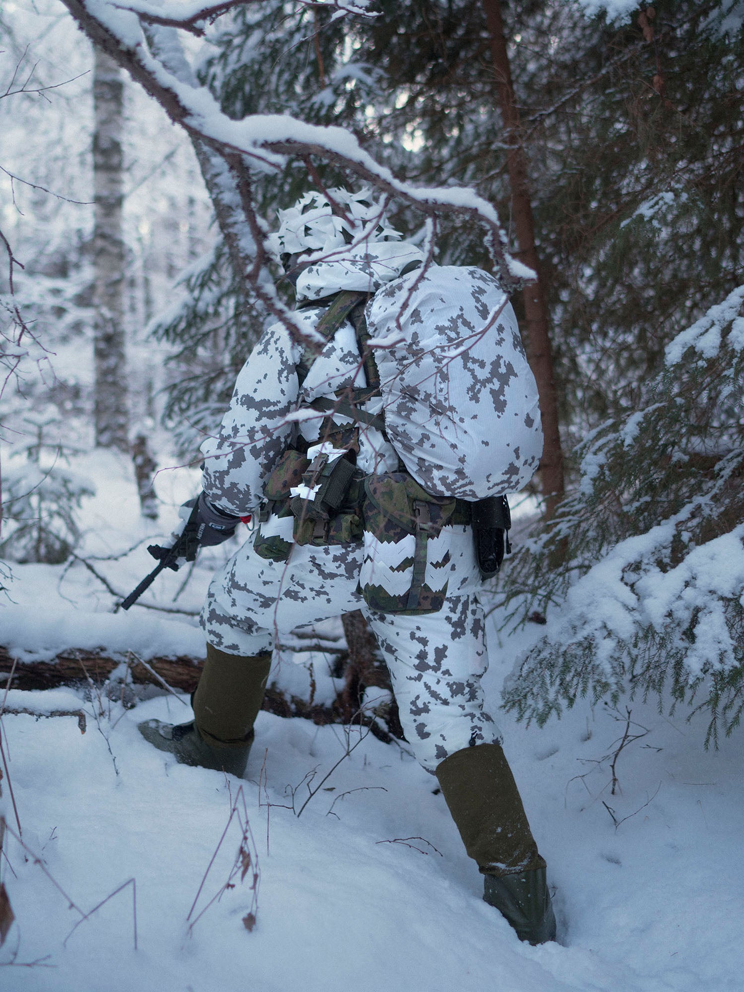 Person in white camouflage gear with a Savotta Lidded GP pouch 4x5 walking through a snowy forest