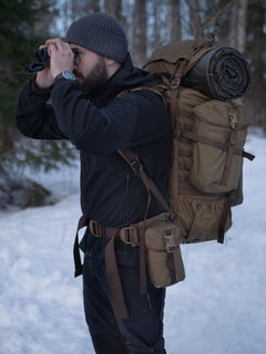 Man with binoculars and a Savotta Kantamus backpack with a Savotta Lidded GP pouch 4x5 attached to the side in a snowy forest