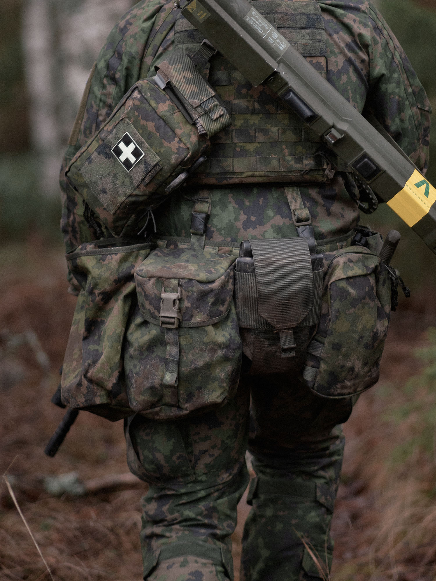 Person wearing a camouflage military uniform with a Savotta Lidded GP pouch 4x5, other pouches and rifle in a forest setting