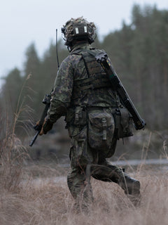 Soldier in camouflage gear with a Savotta Lidded GP pouch 4x5 attached walking through a field with trees in the background