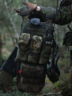 Soldier lifting the Savotta Varjelus plate carrier with Varjelus 3x2 AR15-AK placard and Varjelus groin flap attached in forest setting