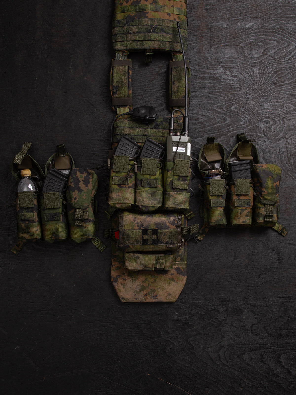Savotta Varjelus PALS placard and different Savotta mag pouches attached to the Varjelus plate carrier which is being spread out on a dark wooden background.