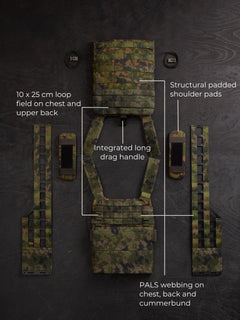 "Savotta Varjelus plate carrier laid out with all its components (cummerbund, shoulder pads and elastic bands) against a dark background. In the background it reads: "10x25 cm loop field on chest and upper back", "Integrated long drag handle", "Structural padded shoulder pads" and "PALS webbing on chest, back and cumerbund".