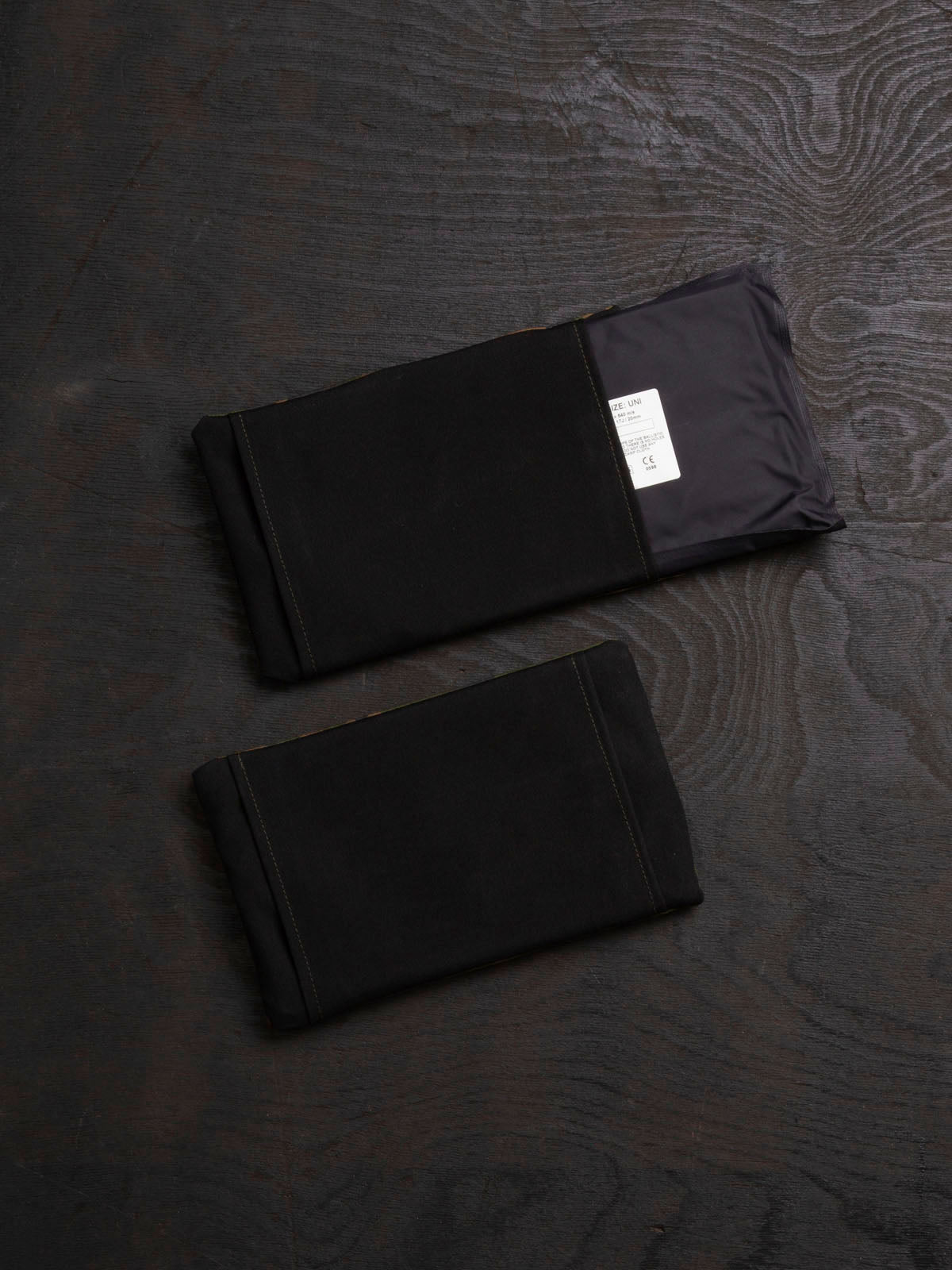 Two Savotta Varjelus side armour bags with Sioen 22,5x14 cm NIJ IIA panels inside of them, on a dark wooden surface