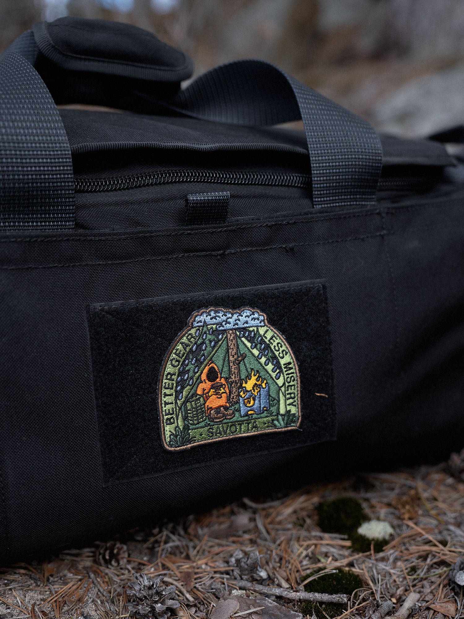 Black Keikka duffel bag with a Savotta Better gear less misery patch on a forest floor