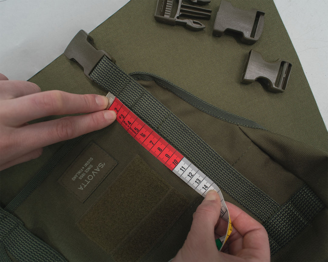 Person measuring a green bag with a ruler, showing close-up details of the bag's strap and hardware.