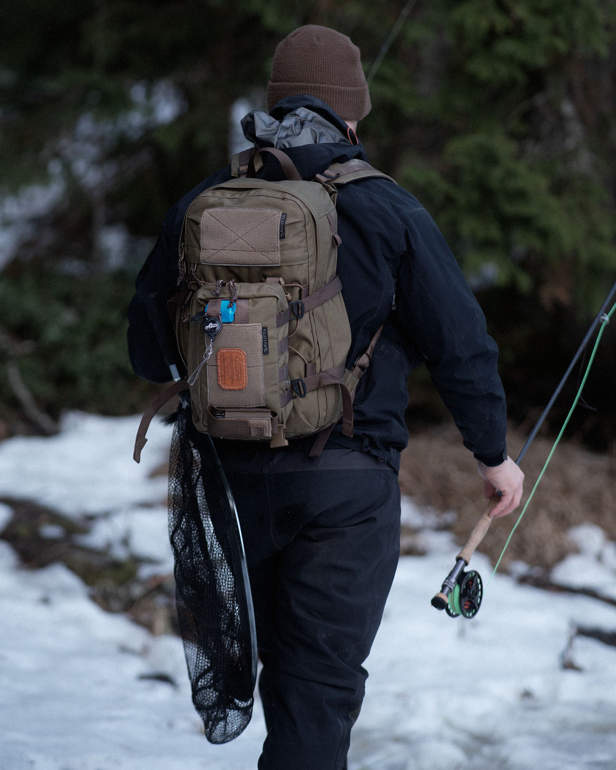 Person with a Savotta Rintamus attached to a Savotta Niukka backpack and fishing gear walking through a snowy forest