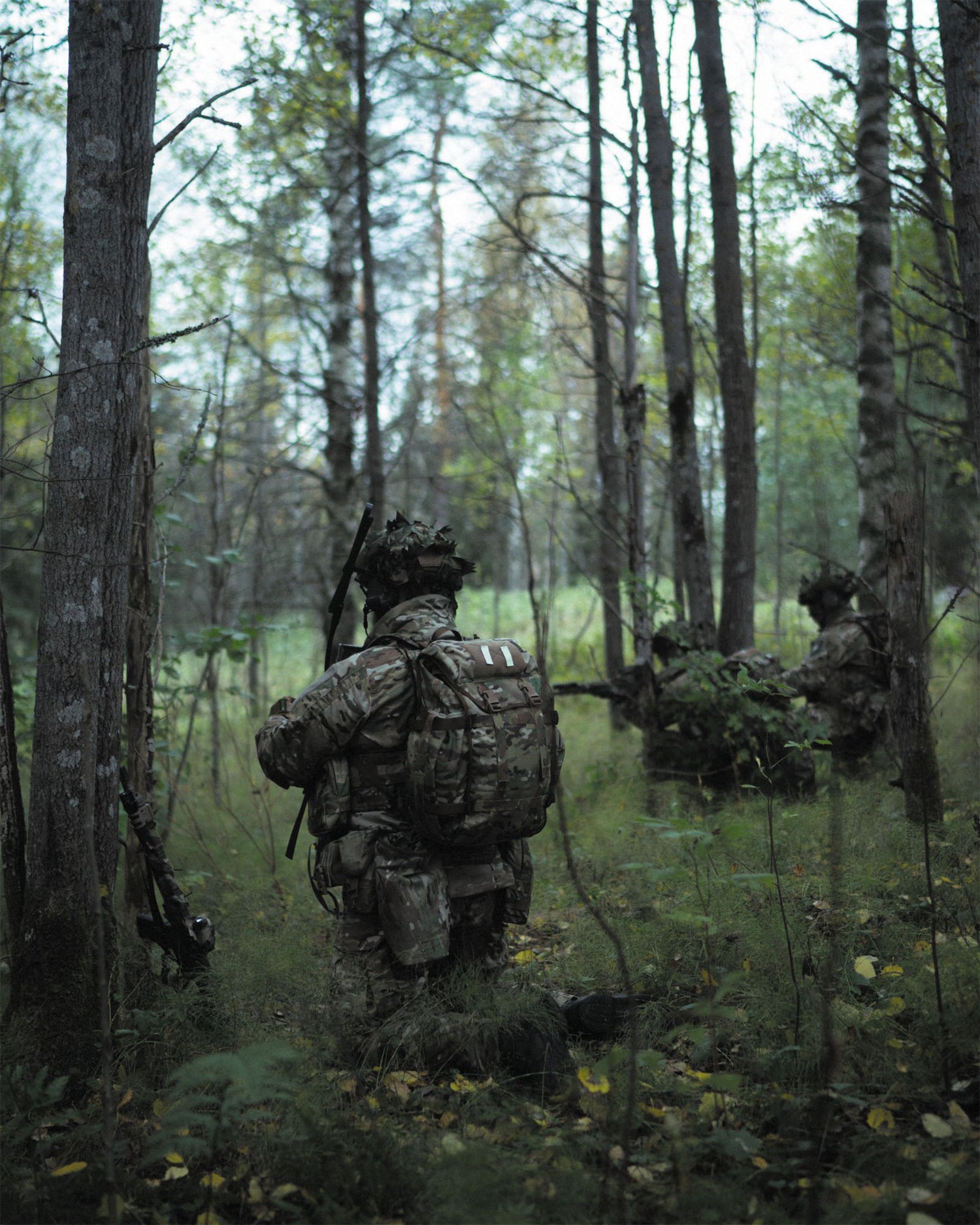 Three soldiers in camouflage gear walking through a forest.